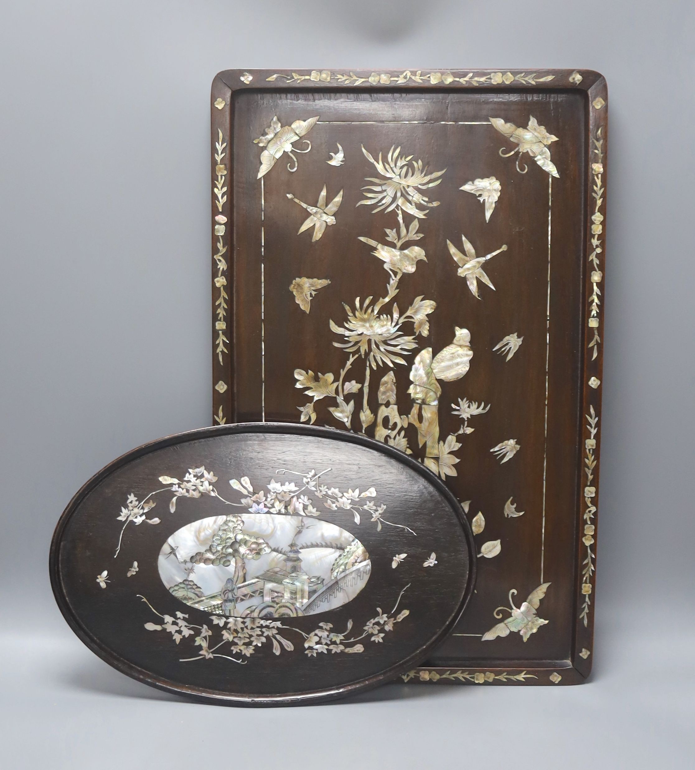 Two Chinese mother of pearl inlaid hongmu trays, the rectangular example with birds and insects amid flowers and the smaller oval example with a pavilion in a landscape within floral sprays 55x34cm